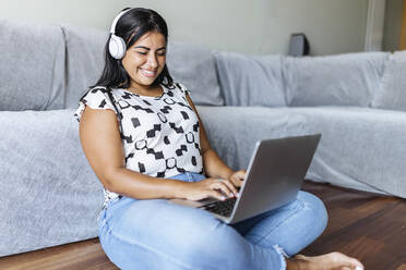 Happy woman using laptop in living room - XLGF02329