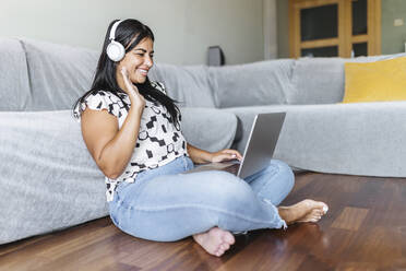 Smiling woman waving during video call through laptop in living room - XLGF02331