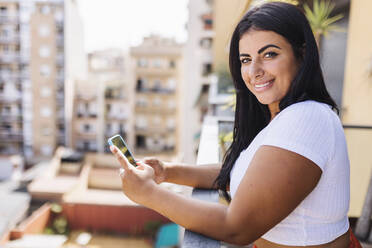 Schöne lächelnde Frau mit Smartphone auf dem Balkon - XLGF02343