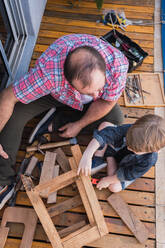 From above unshaven mature dad with attentive boy measuring wooden blocks with tape while spending time on blurred background - ADSF30984