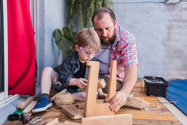 Konzentrierter bärtiger Vater im karierten Hemd mit einem Jungen, der mit Holzklötzen arbeitet - ADSF30996