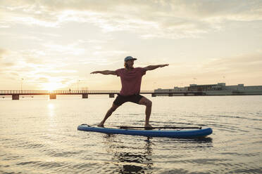 Male instructor with arms outstretched standing on paddleboard in sea - MASF25671