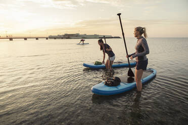 Female friends standing by paddleboard in sea - MASF25673