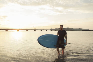 Mann schaut weg und trägt Paddleboard im Meer bei Sonnenuntergang - MASF25674