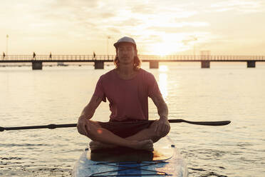 Mann meditiert auf einem Paddelbrett im Meer bei Sonnenuntergang - MASF25677