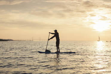 Side view of man rowing paddleboard in sea during sunset - MASF25688
