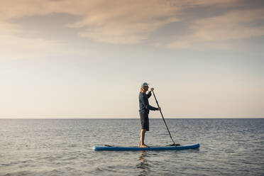 Male instructor paddleboarding in sea during summer vacation - MASF25715