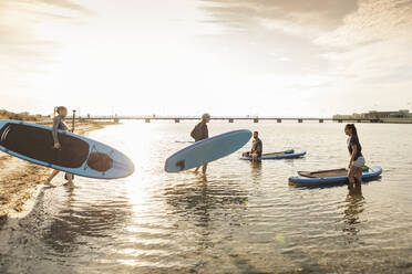 Männliche und weibliche Freunde tragen Paddleboard im Meer - MASF25731