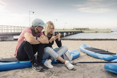 Frau benutzt Smartphone, während ihr Freund auf dem Paddelbrett sitzt - MASF25761