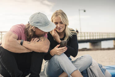 Junge Frau teilt Smartphone mit männlichem Freund am Strand - MASF25762