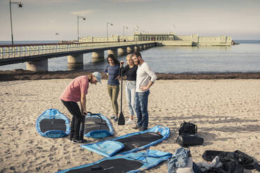 Männlicher Lehrer pumpt Paddleboard mit Freunden am Strand - MASF25771