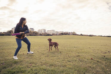 Verspielte junge Frau mit Hund in einem öffentlichen Park - MASF25780