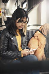 Junge Frau benutzt ein Mobiltelefon, während sie neben ihrem Hund in einer Seilbahn sitzt - MASF25783