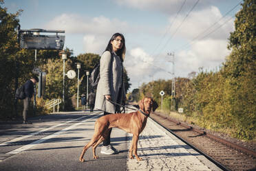 Junge Passagierin und Hund warten am Bahnhof an einem sonnigen Tag - MASF25795