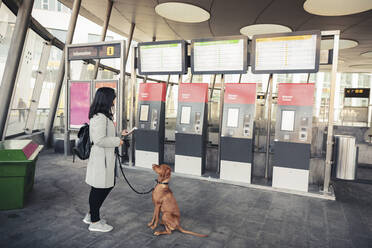 Junge Frau mit Hund am Fahrkartenautomaten im Bahnhof - MASF25808