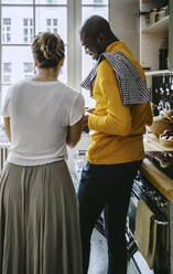 Rear view of mid adult woman standing with boyfriend in kitchen at home - MASF25821