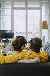 Rear view of girlfriend and boyfriend sitting together on sofa in living room at home - MASF25826