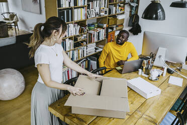 Hohe Winkel Ansicht der männlichen Freiberufler Blick auf glückliche Freundin Öffnung Box stehen am Tisch - MASF25842