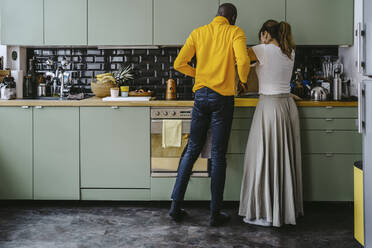 Full length rear view of couple doing chores together in kitchen at home - MASF25846