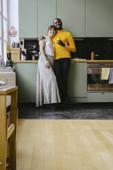 Porträt eines Paares in voller Länge, das zusammen in einer Küche zu Hause steht - MASF25859