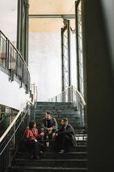 Full length of male and female professionals discussing while sitting on staircase during networking event at convention - MASF25915