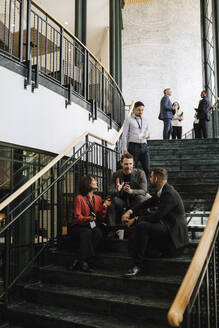 Male and female colleagues discussing on staircase during seminar at convention center - MASF25917