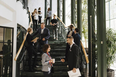 Männliche und weibliche Kollegen diskutieren zusammen, während sie bei einer Networking-Veranstaltung auf der Treppe stehen - MASF25986
