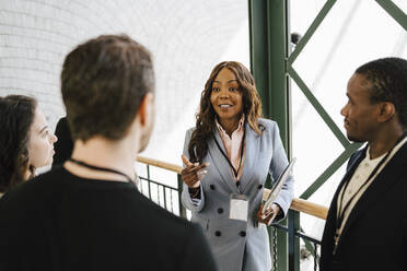 Geschäftsfrau gestikuliert während eines Gesprächs mit männlichen und weiblichen Kollegen bei einer Networking-Veranstaltung - MASF25991