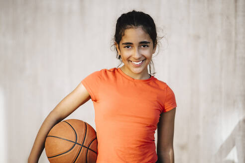 Porträt eines lächelnden Mädchens mit Basketball an der Wand - MASF26030