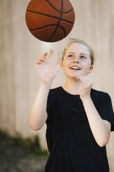 Smiling girl playing with ball at basketball court - MASF26034