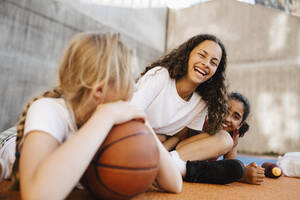 Porträt eines lachenden Mädchens, das mit Freundinnen auf dem Basketballplatz sitzt - MASF26042