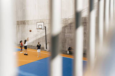 Freundinnen spielen Basketball, gesehen durch das Geländer am Sportplatz - MASF26057