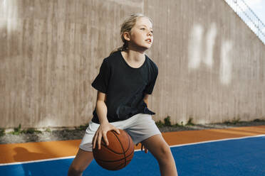 Pre-adolescent girl looking away while playing basketball at sports court - MASF26061