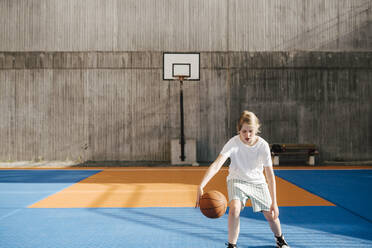 Vorpubertäres Mädchen spielt mit Ball auf einem Basketballplatz - MASF26075