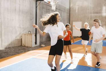 Fröhliche multiethnische Mädchen spielen auf einem Basketballplatz an einem sonnigen Tag - MASF26091