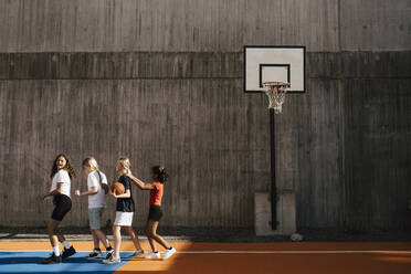 Female friends walking in a row by wall at basketball court - MASF26093