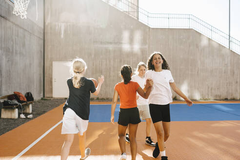 Glückliche Freundinnen halten sich die Hände, während sie auf dem Basketballplatz spazieren gehen - MASF26095