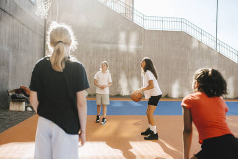 Multi-ethnische Freundinnen spielen Basketball auf einem Sportplatz an einem sonnigen Tag - MASF26097