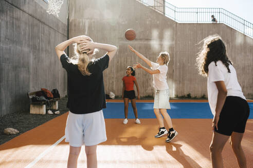 Mädchen wirft Basketball gegen den Reifen, während sie mit Freunden auf dem Platz spielt - MASF26100