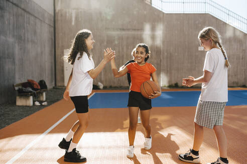 Lächelnde Freundinnen machen High-Five, während sie auf dem Basketballplatz stehen - MASF26101