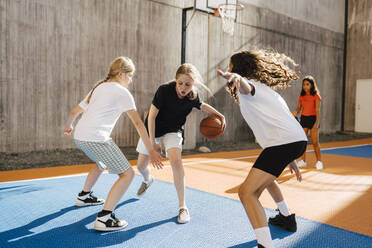 Freundinnen verteidigen ein Mädchen beim Basketballspielen während eines Wettbewerbs auf einem Sportplatz - MASF26102