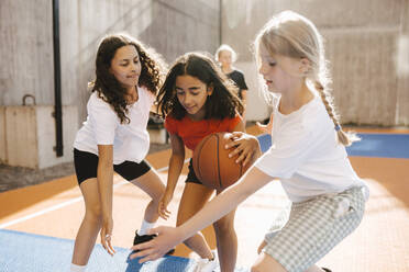 Female friends defending while playing basketball during competition at court - MASF26106