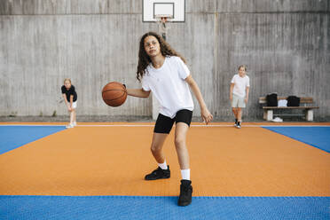 Pre-adolescent girl looking away while practicing basketball in court - MASF26109