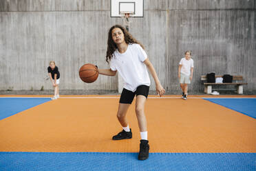 Vorpubertäres Mädchen, das wegschaut, während es auf dem Platz Basketball übt - MASF26109