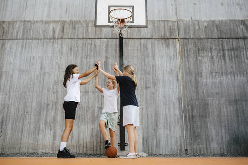 Weibliche Freunde machen High-Five, während sie auf dem Basketballplatz stehen - MASF26112