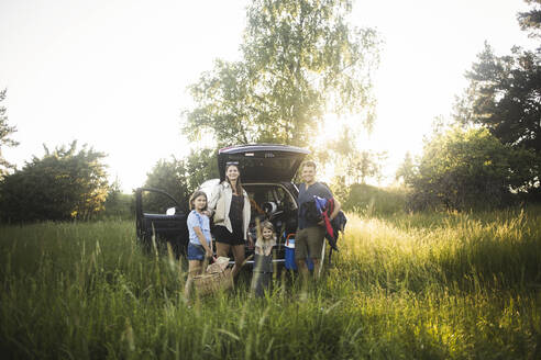 Porträt einer Mutter, eines Vaters und zweier Töchter, die neben einem Auto an einer Ladestation für Elektrofahrzeuge stehen - MASF26144
