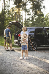 Porträt einer Mutter, eines Vaters und zweier Töchter, die neben einem Auto an einer Ladestation für Elektrofahrzeuge stehen - MASF26160