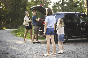 Porträt einer Mutter, eines Vaters und zweier Töchter, die neben einem Auto an einer Ladestation für Elektrofahrzeuge stehen - MASF26162