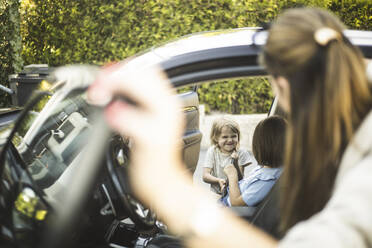 Portrait of mother, father and two daughters standing by car at electric vehicle charging station - MASF26166