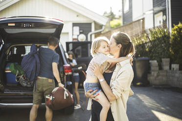 Portrait of mother, father and two daughters standing by car at electric vehicle charging station - MASF26171